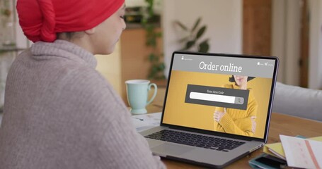Poster - Biracial woman at table using laptop, shopping online for fashions, slow motion
