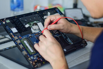 computer technician A laptop motherboard repairman is using an IC meter to find defects on the motherboard to repair on his table. Board repair using modern technology