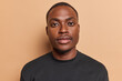 © wayhome.studio  - People and positive emotions concept. Indoor close up of young happy satisfied African american male standing in centre isolated on beige background looking straight at camera dressed in black t shirt