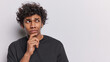 Studio portrait of young thoughtful Hindu man standing on left on white background in black t shirt keeping hand on chin with blank space for your advertisement trying to solve difficult problem