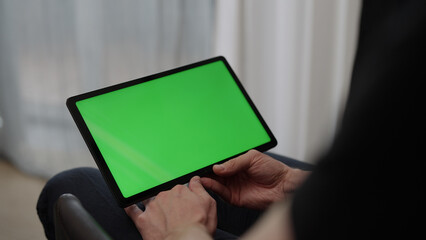 Wall Mural - Man sitting indoors on a chair with tablet pc with green screen