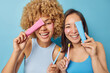 Horizontal shot of positive women undergo daily dantal procedures hold toothpaste and toothbrush over faces dressed in casual t shirts smile broadly isolated over blue background. Oral care concept