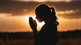 Fototapeta Dmuchawce - Silhouette of a praying girl with folded palms at sunset