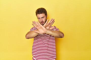 Young Caucasian man on a yellow studio background doing a denial gesture