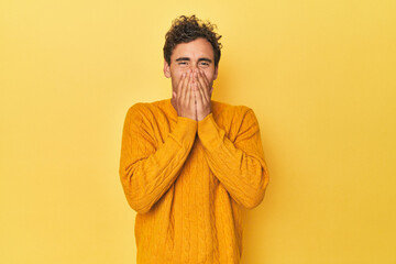 Wall Mural - Young Latino man posing on yellow background laughing about something, covering mouth with hands.