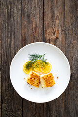 Wall Mural - Seared cod loin and sliced lemon on wooden table
