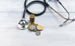 A pile of coins lies on the table and  a stethoscope.