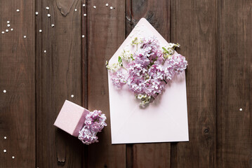 Sticker - Square postage envelope and small gift box on wooden background, bouquet of lilac. Flat lay, top view. Happy mother's day, women's day or birthday, wedding composition. Blank greeting card, mockup