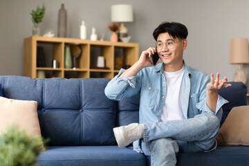 Poster - Japanese young man smiling talking on smartphone sitting at home