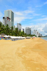 Wall Mural - Nha Trang city, Vietnam - October 18, 2023 : overlooking the beautiful coast of Nha Trang with palm trees on the beach with deck chair and parasol