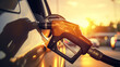 A man's hand firmly grasps the gas pump nozzle as he refuels his car, offering a close-up view of the refueling process against the backdrop of the gas station. 