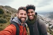 © Good Shot - Couple of men of different nationalities take selfie on their phone and smile at the top of the mountain