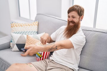 Wall Mural - Young redhead man watching movie sitting on sofa at home