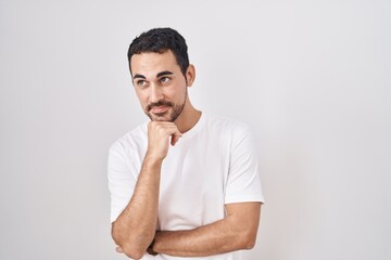 Sticker - Handsome hispanic man standing over white background looking confident at the camera smiling with crossed arms and hand raised on chin. thinking positive.