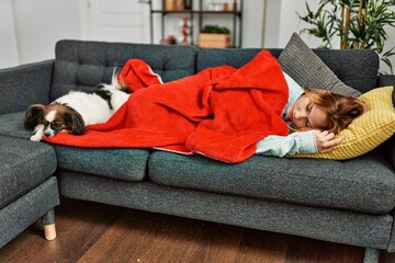 Poster - Young caucasian woman lying on sofa sleeping with dog at home