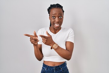 Wall Mural - Beautiful black woman standing over isolated background pointing aside worried and nervous with both hands, concerned and surprised expression