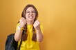 Young caucasian woman wearing student backpack over yellow background angry and mad raising fists frustrated and furious while shouting with anger. rage and aggressive concept.