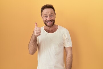 Poster - Middle age man with beard standing over yellow background doing happy thumbs up gesture with hand. approving expression looking at the camera showing success.