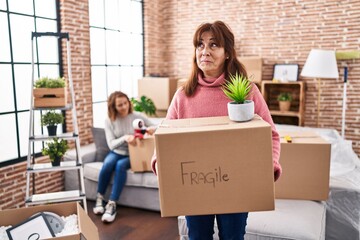 Canvas Print - Mother and daughter moving to a new home holding cardboard box smiling looking to the side and staring away thinking.