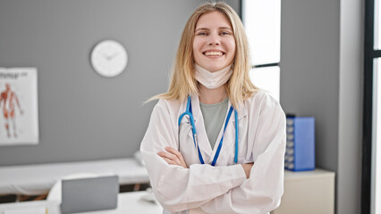 Poster - Young blonde woman doctor standing with arms crossed gesture taking medical mask off at clinic