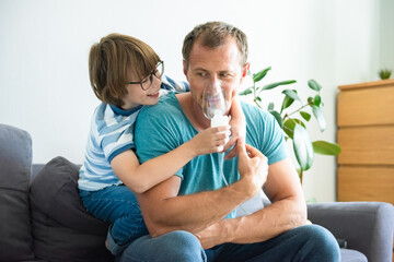 happy child boy treats his dad at home. medical procedures. inhaler. respiratory medicine. home trea