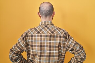 Canvas Print - Young hispanic man with tattoos standing over yellow background standing backwards looking away with arms on body