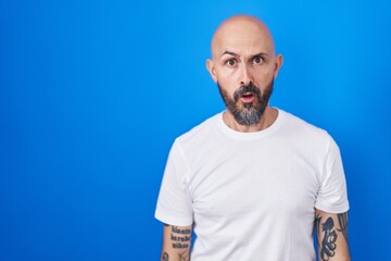 Poster - Hispanic man with tattoos standing over blue background in shock face, looking skeptical and sarcastic, surprised with open mouth