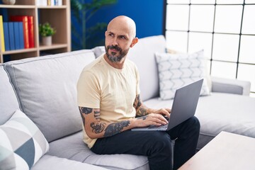 Wall Mural - Young bald man using laptop sitting on sofa at home