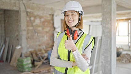 Wall Mural - Young blonde woman architect standing with arms crossed gesture doing thumb up gesture at construction site