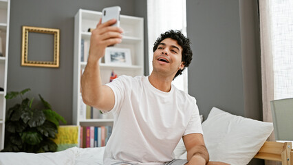 Poster - Young latin man doing video call sitting on the bed at bedroom