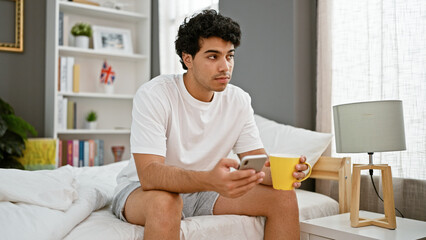 Poster - Young latin man using smartphone drinking coffee at bedroom