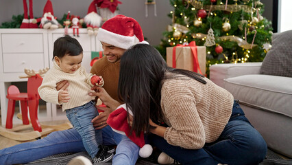 Poster - Couple and son holding decoration ball sitting on floor by christmas tree at home