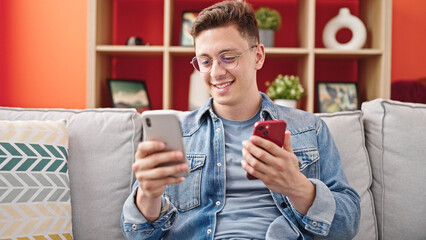 Poster - Young hispanic man using smartphones sitting on sofa at home