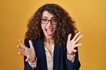 Sticker - Hispanic woman with curly hair standing over yellow background celebrating crazy and amazed for success with arms raised and open eyes screaming excited. winner concept