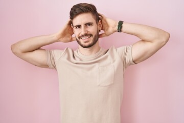 Poster - Hispanic man with beard standing over pink background relaxing and stretching, arms and hands behind head and neck smiling happy