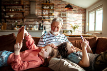 Grandfather bonding with his grandchildren while they use electronics on the couch at home