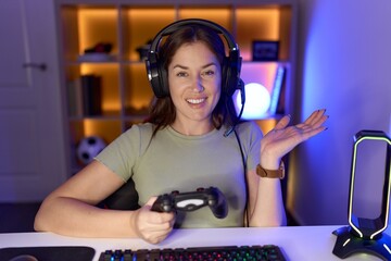 Sticker - Beautiful brunette woman playing video games wearing headphones pointing aside with hands open palms showing copy space, presenting advertisement smiling excited happy