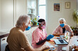 © Marko Geber - Young African American caregiver consulting a doctor on a video call on the laptop with her senior patients at home