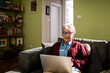 © Marko Geber - Senior woman using a laptop on the couch at home