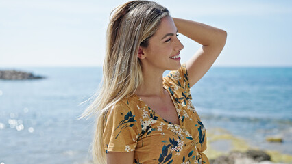 Poster - Young blonde woman smiling confident combing hair at seaside