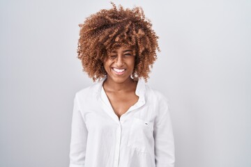 Sticker - Young hispanic woman with curly hair standing over white background winking looking at the camera with sexy expression, cheerful and happy face.