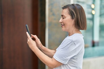 Wall Mural - Middle age woman smiling confident using smartphone at street