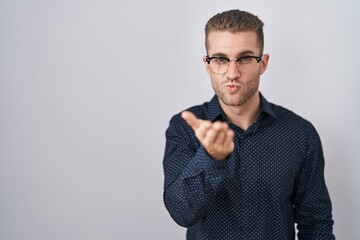 Sticker - Young caucasian man standing over isolated background looking at the camera blowing a kiss with hand on air being lovely and sexy. love expression.