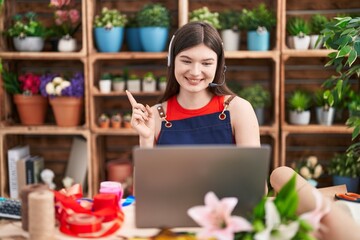 Wall Mural - Young caucasian woman working at florist shop doing video call smiling happy pointing with hand and finger to the side