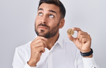 Wall Mural - Handsome hispanic man holding litecoin cryptocurrency coin serious face thinking about question with hand on chin, thoughtful about confusing idea