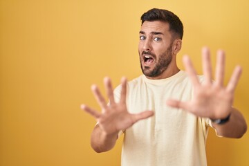 Sticker - Handsome hispanic man standing over yellow background afraid and terrified with fear expression stop gesture with hands, shouting in shock. panic concept.