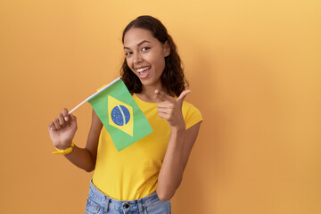 Wall Mural - Young hispanic woman holding brazil flag pointing fingers to camera with happy and funny face. good energy and vibes.