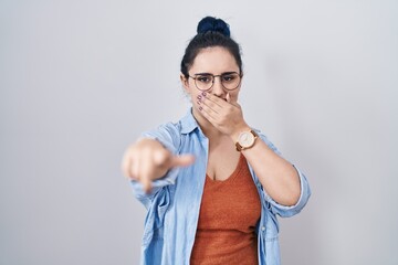 Wall Mural - Young modern girl with blue hair standing over white background laughing at you, pointing finger to the camera with hand over mouth, shame expression