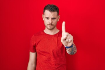 Canvas Print - Young hispanic man standing over red background pointing with finger up and angry expression, showing no gesture