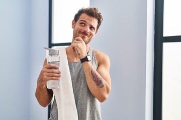 Canvas Print - Young hispanic man wearing sportswear drinking water with hand on chin thinking about question, pensive expression. smiling with thoughtful face. doubt concept.